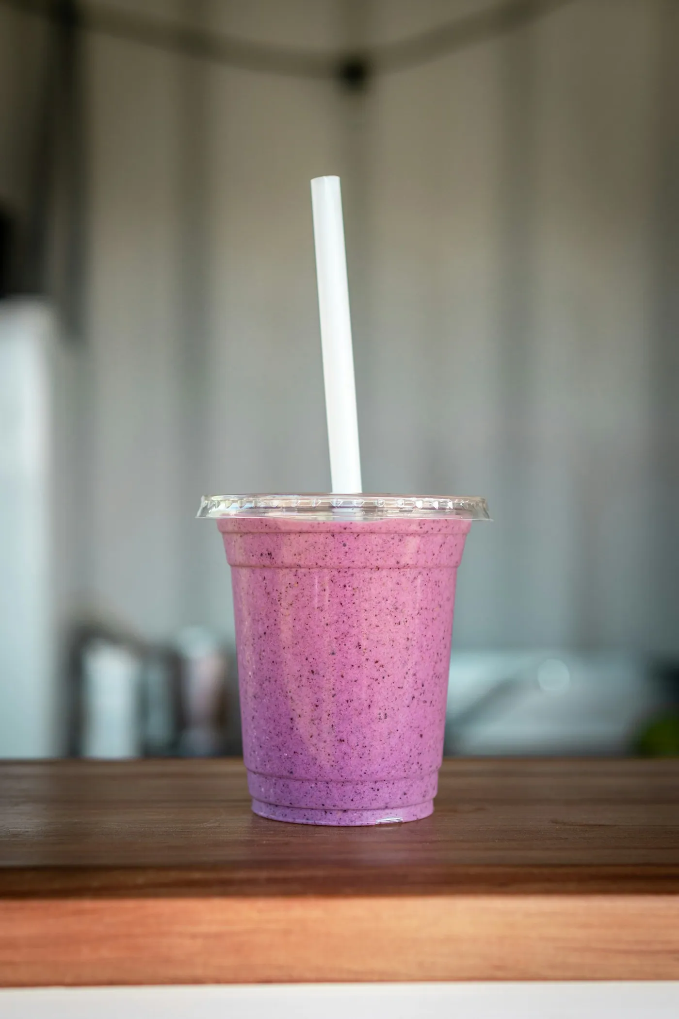 Smoothie roxo em copo plástico com canudo sobre balcão de madeira