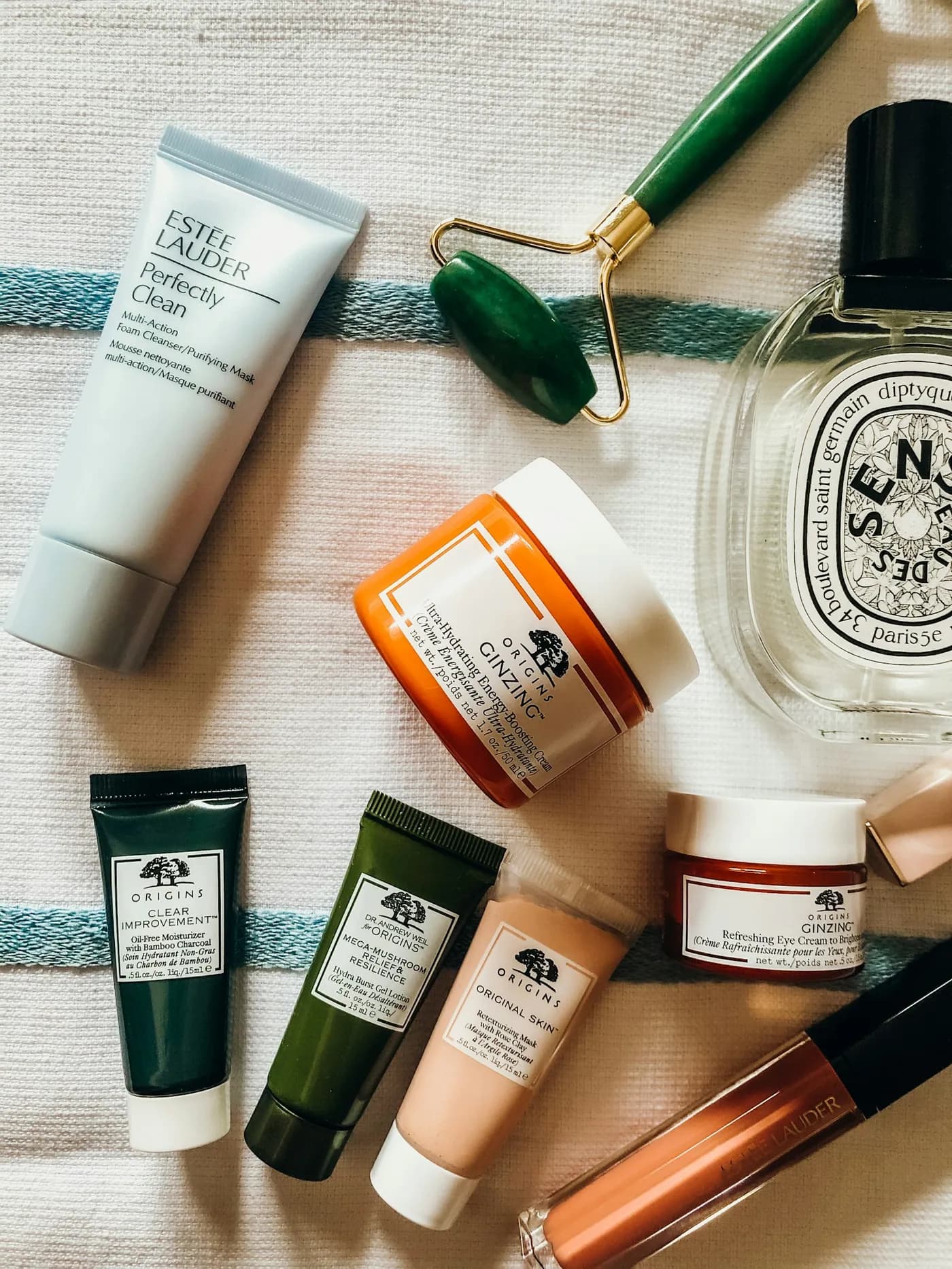 Bisnagas e potes de creme facial espalhados sobre tecido claro, ao lado de um rolo facial verde