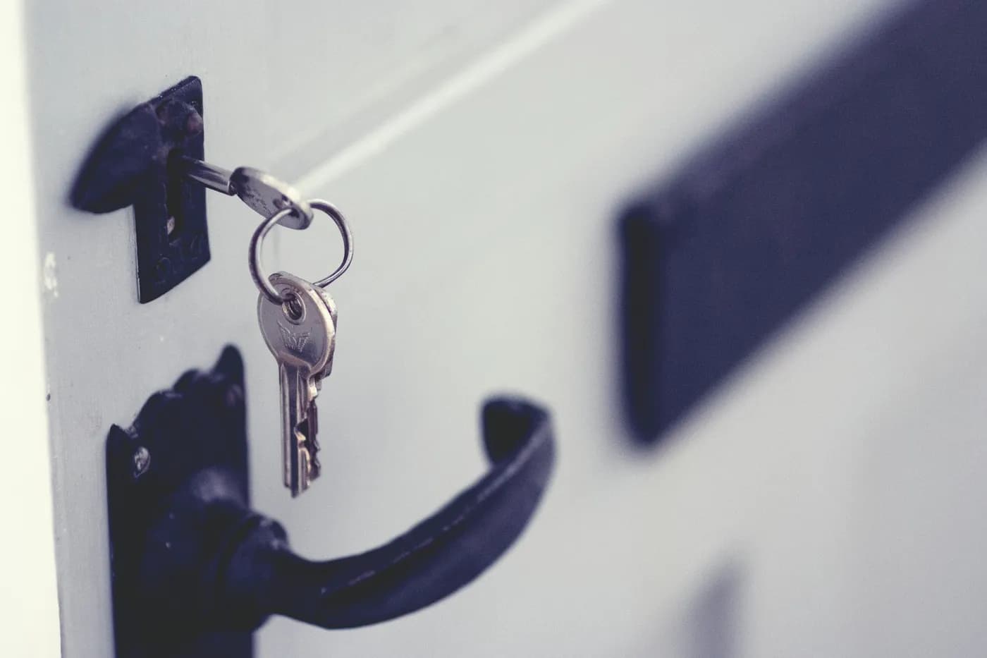 Chave com chaveiro pendurada na fechadura de uma porta branca com maçaneta preta