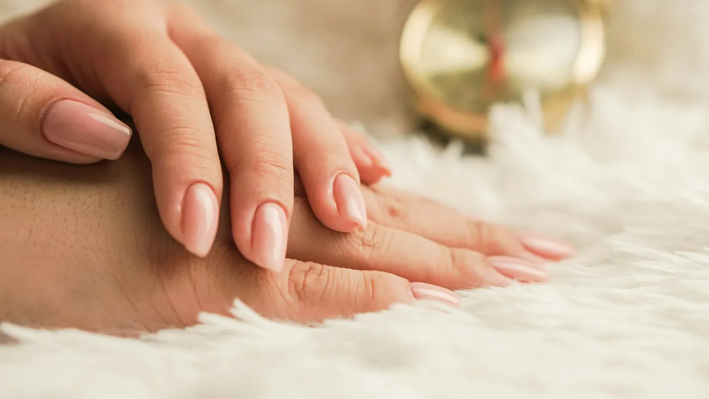Mãos entrelaçadas mostrando unhas naturais bem cuidadas com esmalte rosa claro