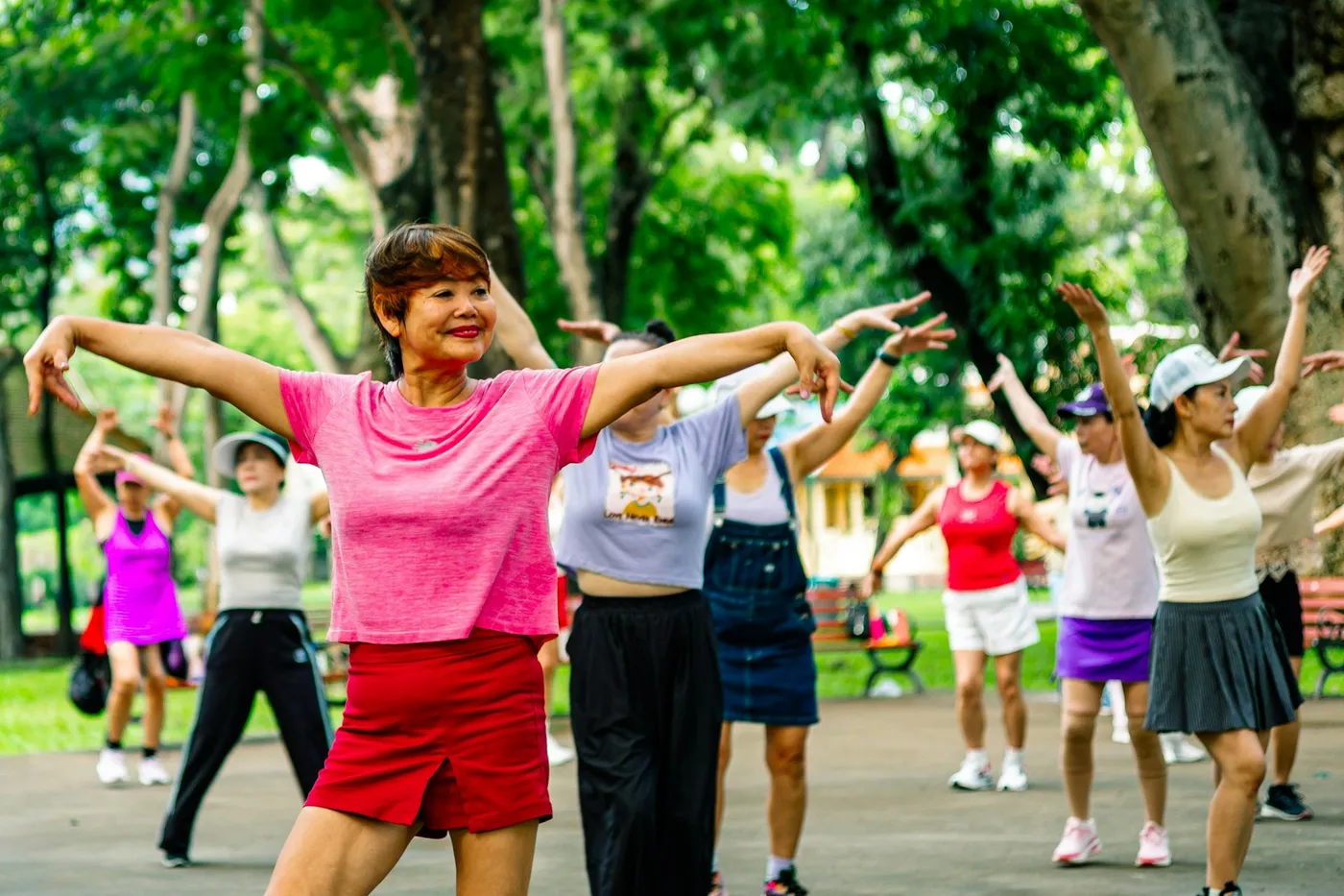 Grupo de mulheres de várias idades fazendo ginástica ao ar livre em um parque arborizado, de braços abertos