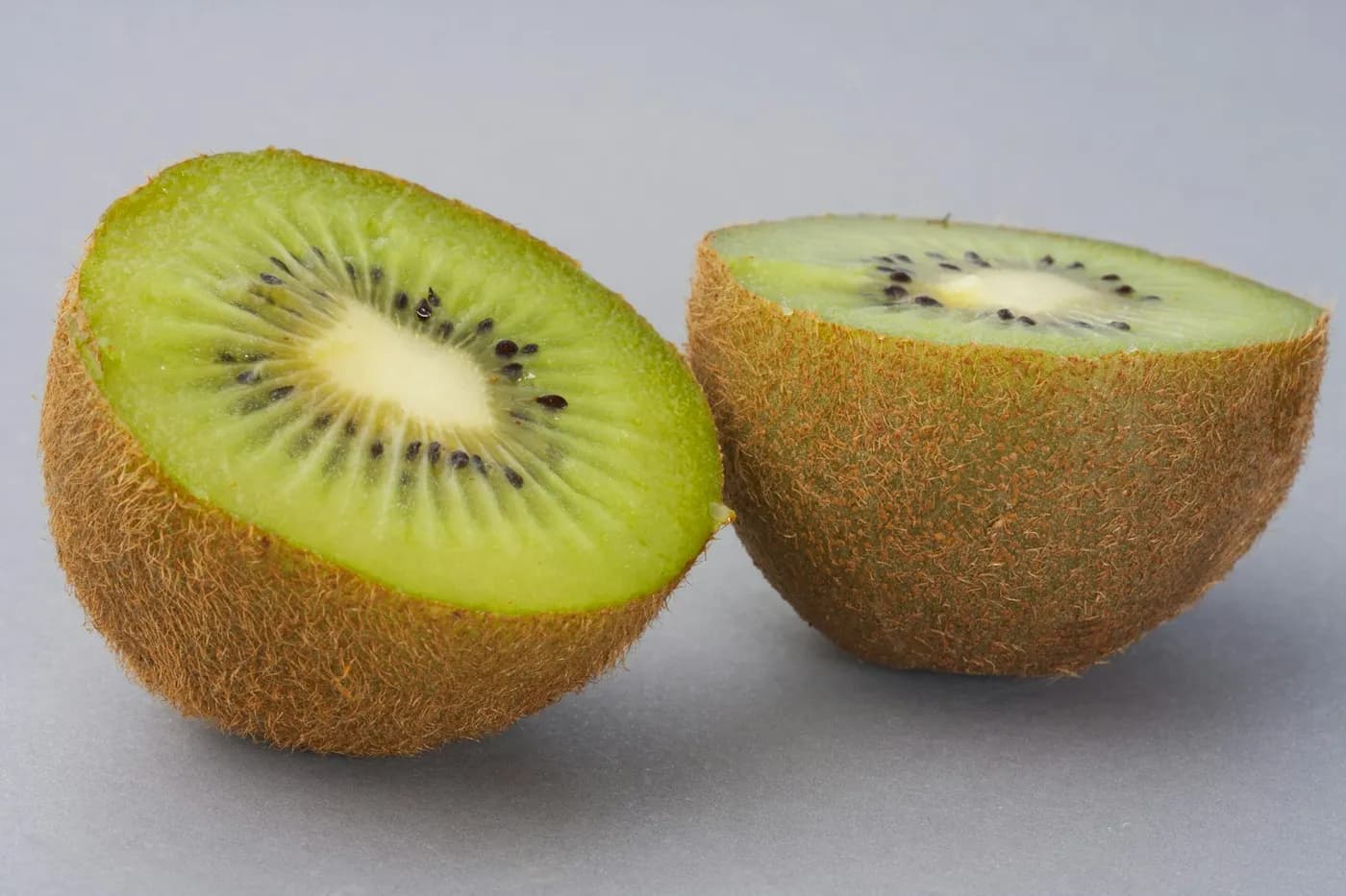 Duas metades de kiwi com polpa verde e sementes pretas sobre fundo cinza
