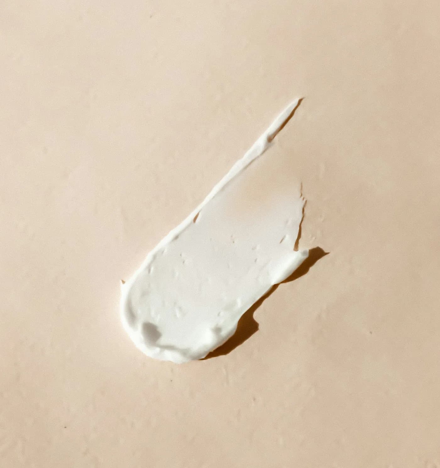 Textura de creme branco espalhado sobre superfície bege clara, em close