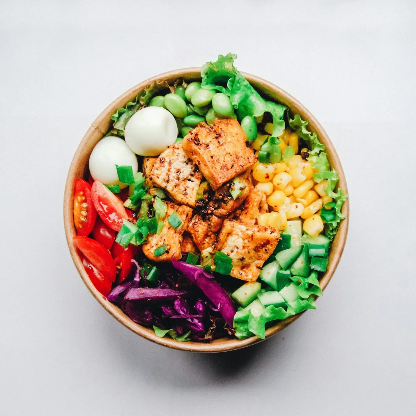 Tigela vista de cima com tofu grelhado, milho, edamame, ovos de codorna, tomate e repolho roxo