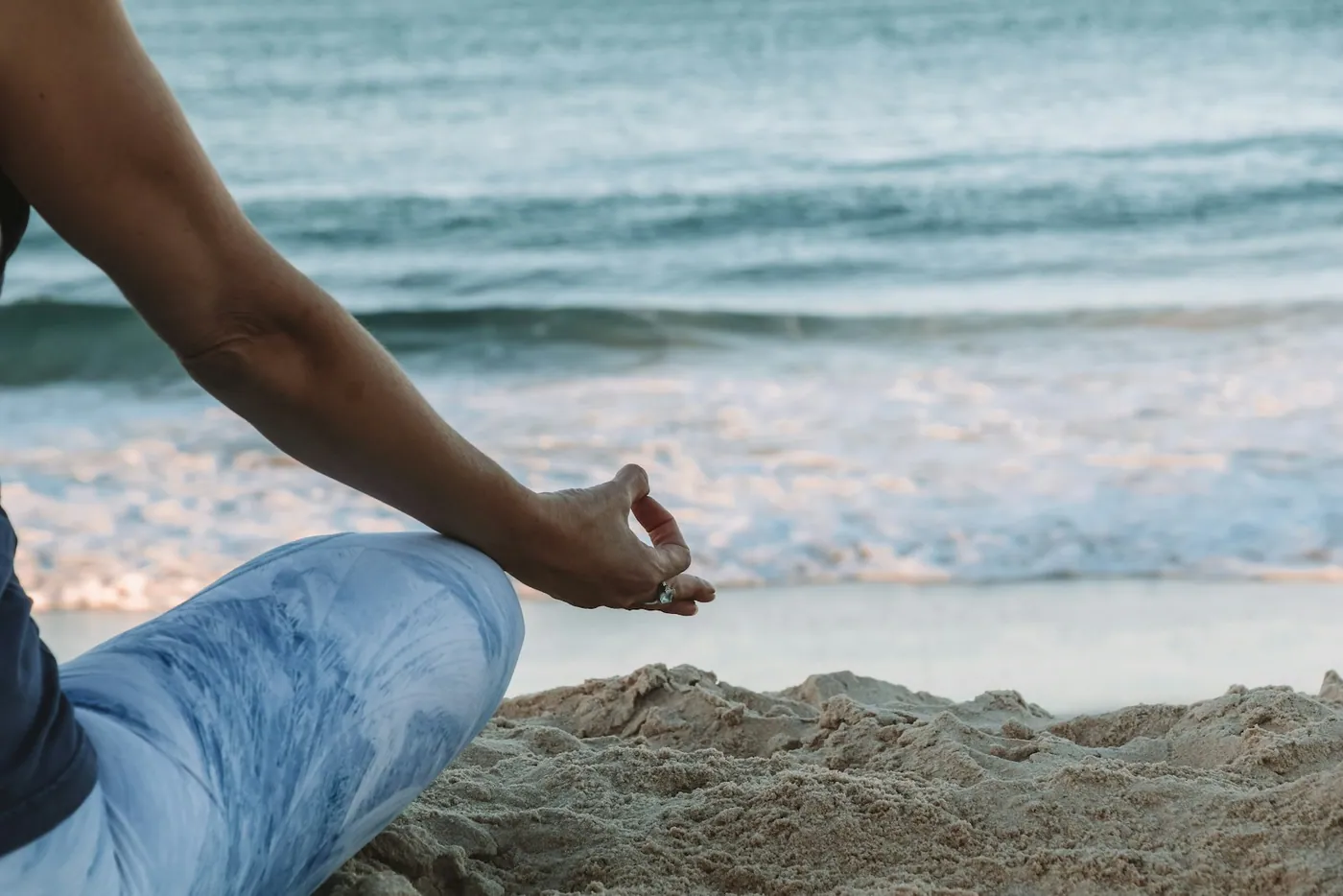 Pessoa sentada em meditação na areia à beira-mar