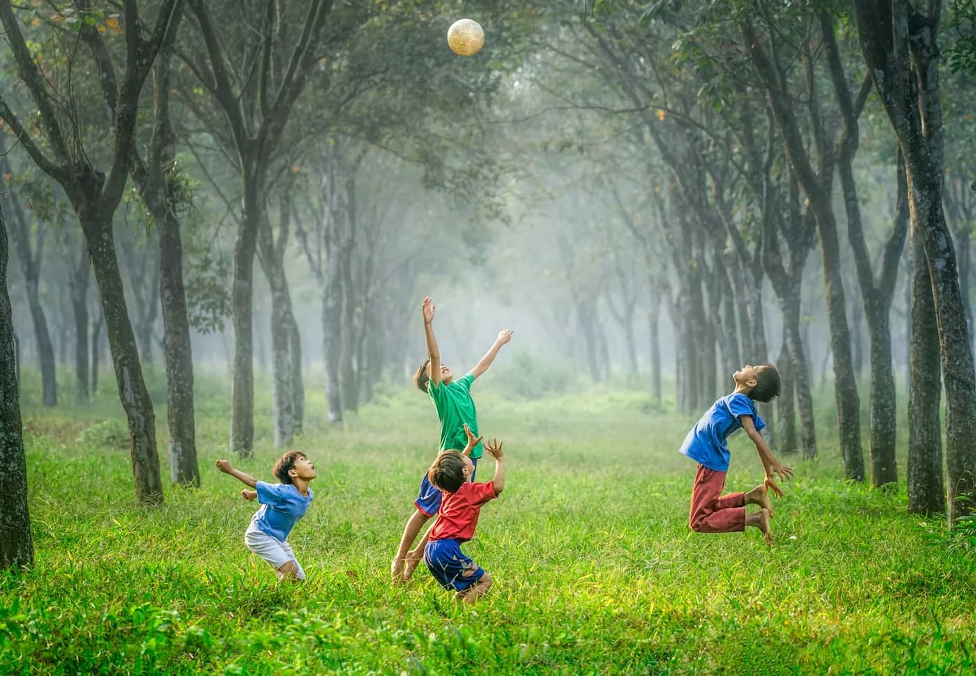 Crianças correndo e brincando com bola entre árvores