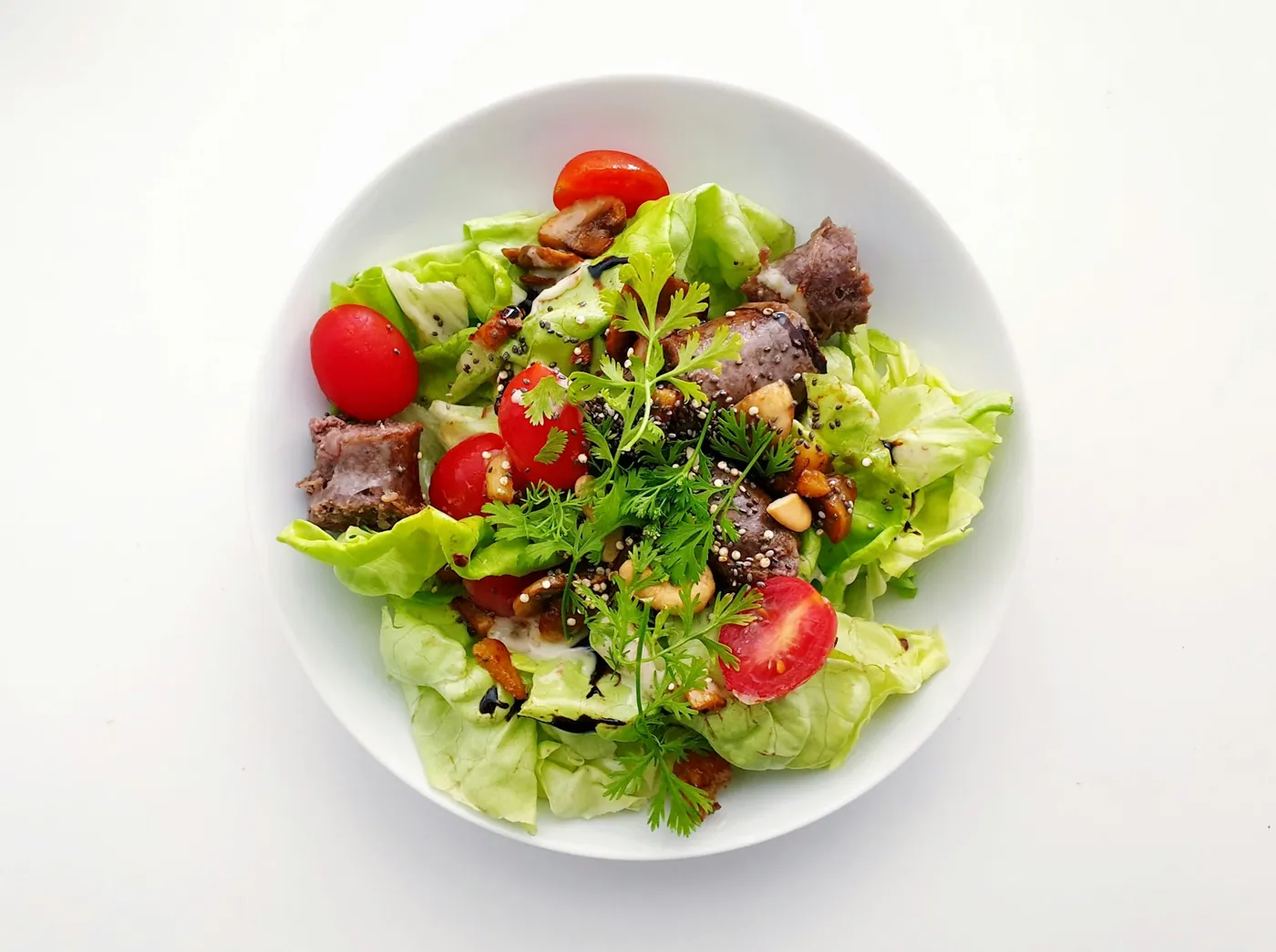 Salada de folhas com tomate, carne e castanhas em prato branco, vista de cima