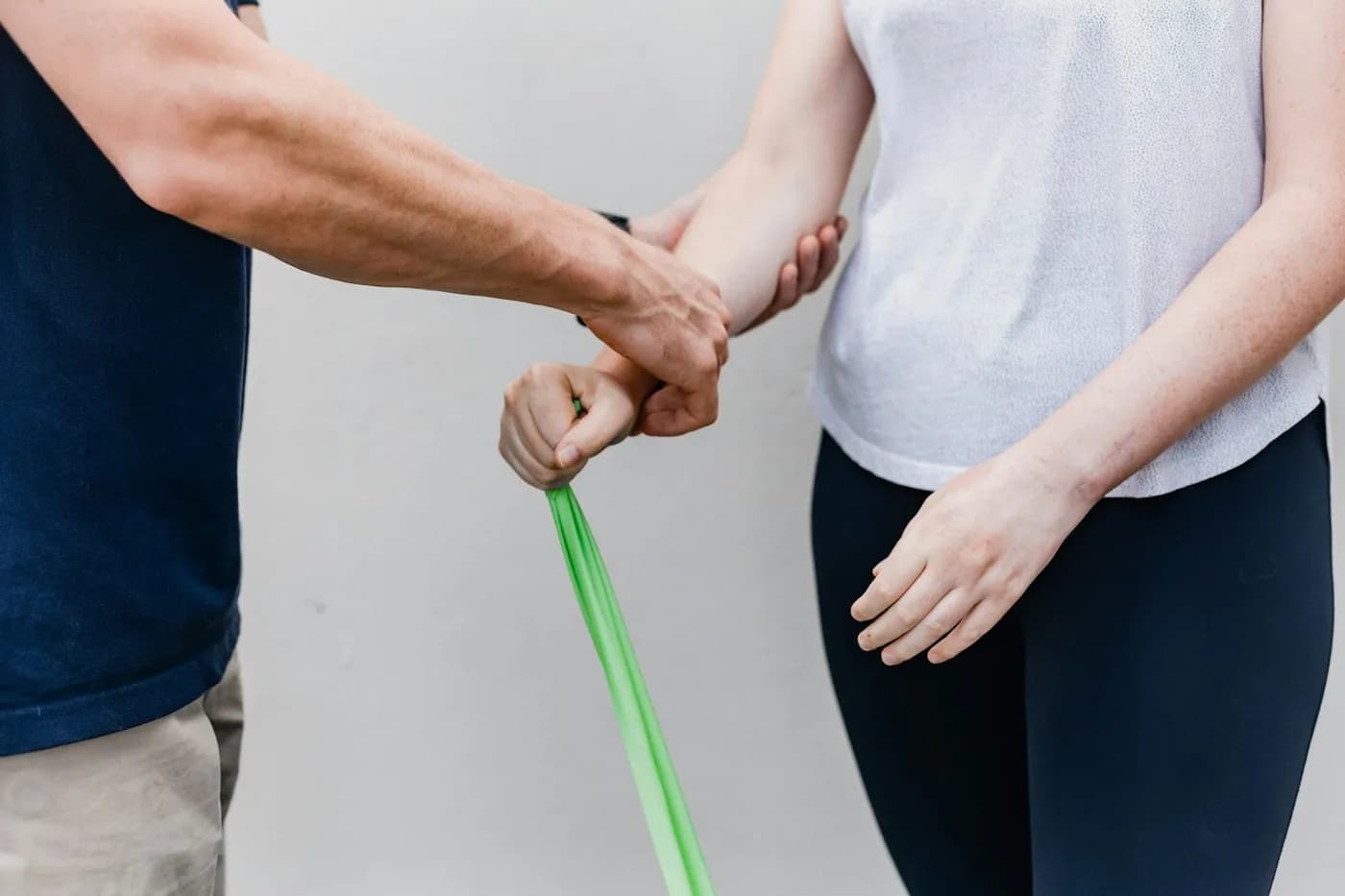 Profissional de camiseta azul segurando o pulso de uma mulher que puxa uma faixa elástica verde durante um exercício