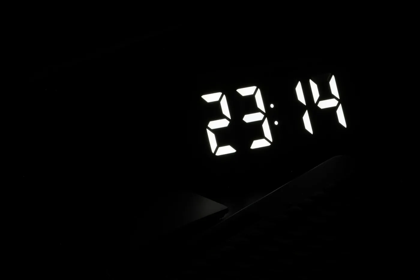 Relógio digital marcando 23:14 em números brancos acesos num quarto totalmente escuro
