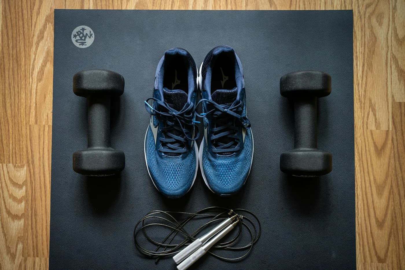 Par de halteres, tênis e corda de pular sobre um tapete de exercício